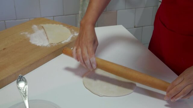 A woman rolls out a piece of dough with a wooden rolling pin on a white kitchen counter. She feels energetic, focused, and content during her cozy afternoon home baking routine.