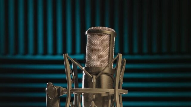 Slow motion colorful studio shot of voiceover dialogue podcast microphone on stand in close-up detail with acoustic foam in recording space with dark background and bright lighting of broadcast vo mic
