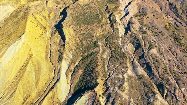 Aerial top-down view of colorful mountain terrain with steep ridges, eroded slopes, and sparse vegetation. Ideal for geology and nature travel concepts.