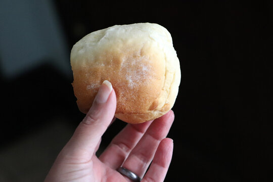 Holding homemade golden yeast dinner roll bun against dark background