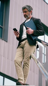 Video of mature elegant businessman using smartphone while staying in front of office