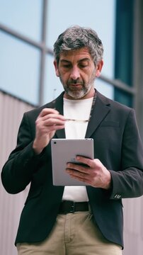 Video of mature elegant businessman working with digital tablet while staying in front of office