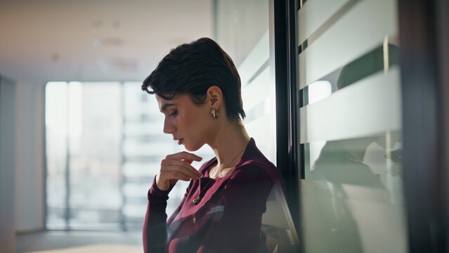 Pensive woman leaning office glass wall. Worried businesswoman thinking work