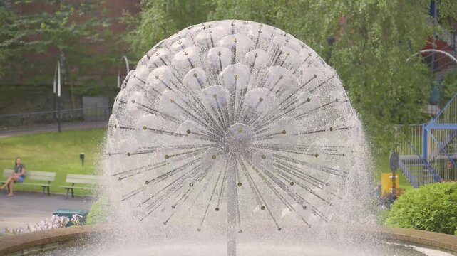 Spherical fountain sculpture spraying water in green urban park