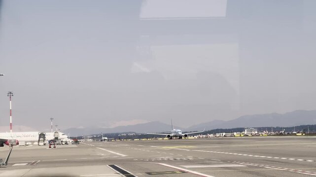 Commercial passenger airplane taxiing on the airport tarmac. Preparing for takeoff on a hazy day with a special vehicle for disabled passengers passing by. All framed by an interior window reflection