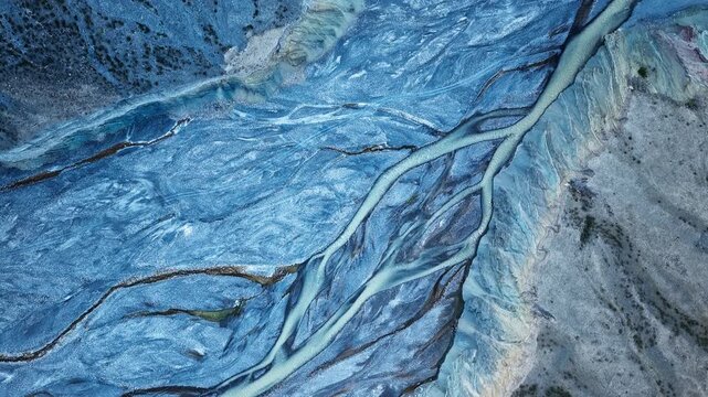 Aerial top down view of glacial braided river channels flowing through a vivid blue sediment landscape in Xinjiang, China.