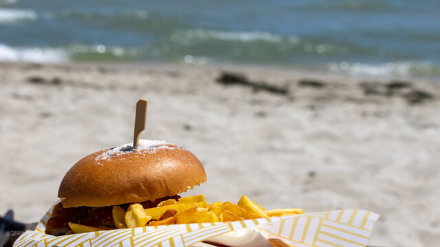 Delicious burger and french fries served on a beach with sea background