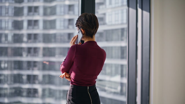 Pensive woman talking phone office window. Back view business call closeup.