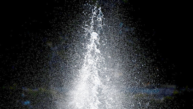 Dynamic close-up capture of a powerful vertical water fountain jet splashing against a dark nocturnal background creating beautiful crystalline spray