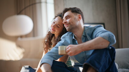 Obraz premium Smiling couple cuddling coffee cups sofa. Affectionate pair relaxing weekend