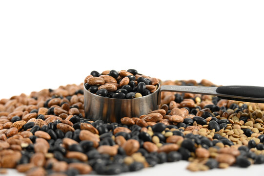 Several types of beans filling a silver measuring cup that is sitting in a pile of black and pinto beans