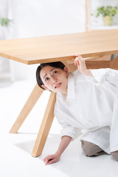 地震が起きてテーブルの下に隠れる女性