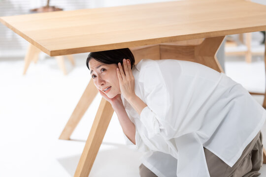 地震が起きてテーブルの下に隠れる女性