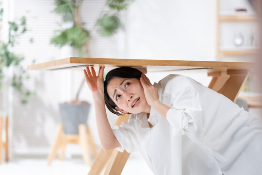地震が起きてテーブルの下に隠れる女性