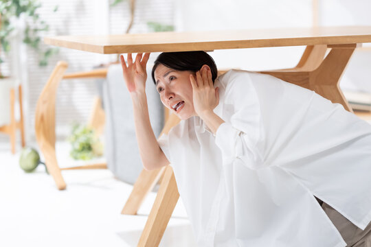 地震が起きてテーブルの下に隠れる女性