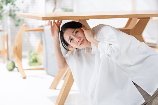 地震が起きてテーブルの下に隠れる女性