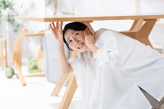 地震が起きてテーブルの下に隠れる女性