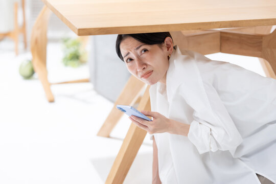 地震が起きてテーブルの下に隠れる女性