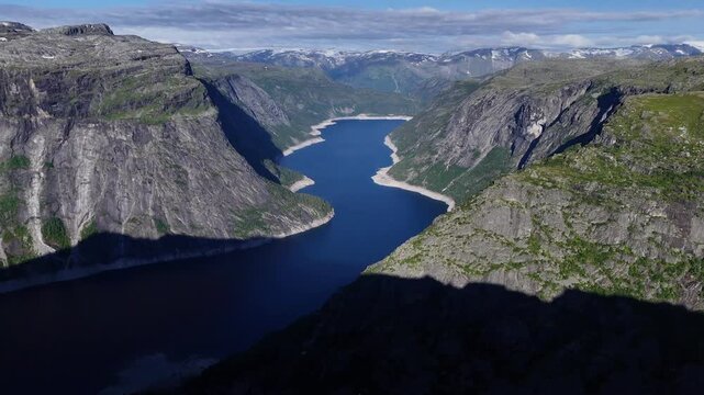 Drone view over deep blue fjord lake and steep rocky cliffs in the Norwegian mountains on a clear summer day.