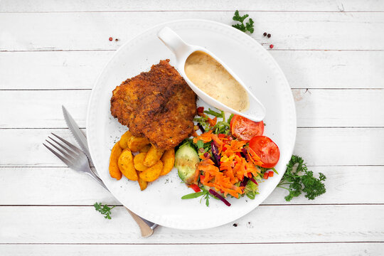 Classic German Jagerschnitzel with a mushroom cream sauce, potato wedges and salad. Top view table scene against a white wood background.