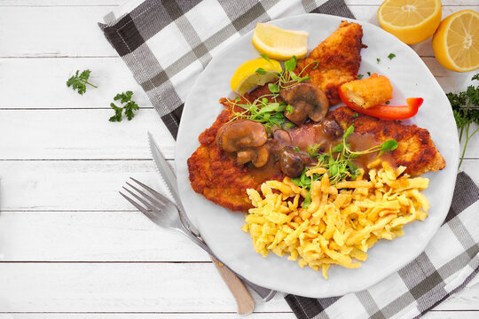 German Jagerschnitzel with a brown mushroom gravy and spaetzle noodles. Top view table scene against a white wood background.