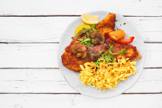Traditional German Jagerschnitzel with a brown mushroom gravy and spaetzle noodles. Top down view on a white table background.