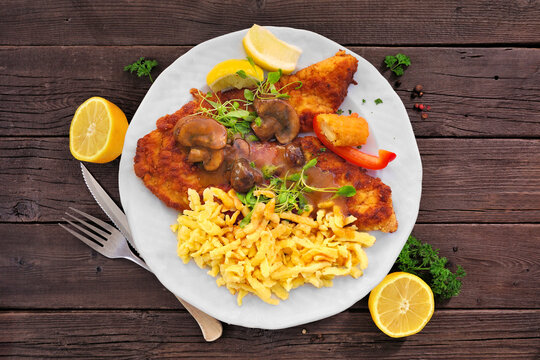 German Jagerschnitzel with a brown mushroom gravy and spaetzle noodles. Above view table scene on a dark wood background.