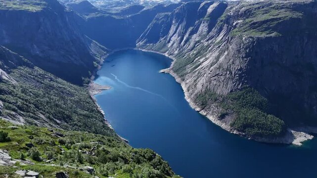 Drone panorama of deep blue fjord lake framed by steep rocky mountains and green slopes in summer, Hardanger, Norway.