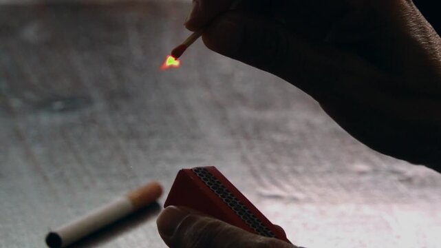 close-up slow motion video of a hand lighting a cigarette with a match, preparing to smoke