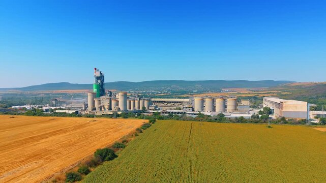 Industrial plant behind agricultural fields. A wide aerial shot shows a large manufacturing facility situated beyond expansive yellow and green fields.