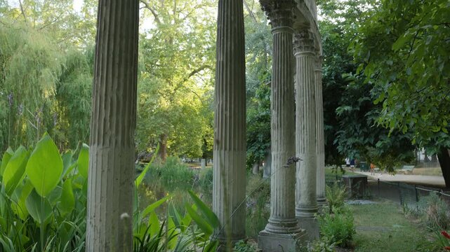 Camera Tilting Up View of Classical Stone Columns along a Lush Park Path and Pond