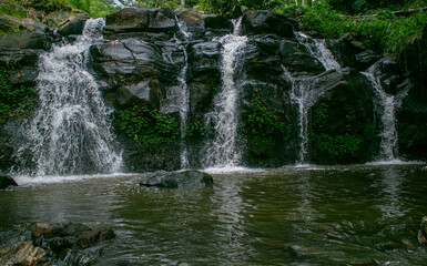 A scenic tropical waterfall cascading over dark volcanic rocks, surrounded by lush green bamboo and dense rainforest vegetation in Indonesia. Captured with a long exposure technique, the silky flowing © Eriec