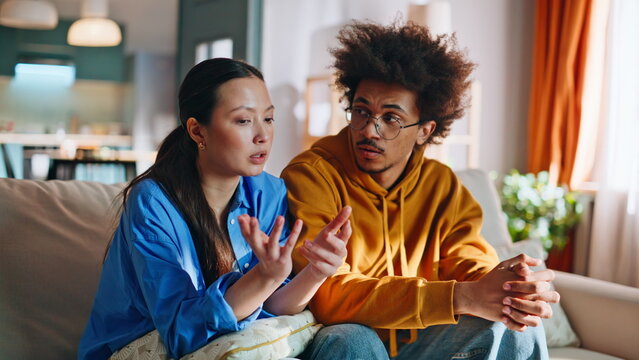 Multiracial couple arguing on sofa. Upset woman crying boyfriend comforting her.
