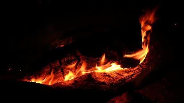 fiery arc of flame curves around dark log on campfire place under open night sky