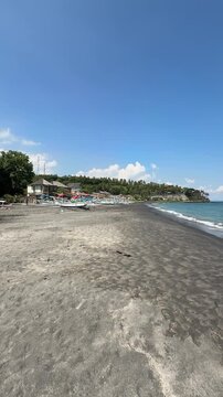 Tropical black sand beach with traditional jukung boats and coastal village