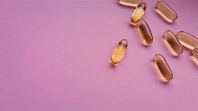 Golden vitamin D3 gel capsules on pink background for wellness concept