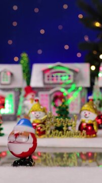 Ahead of a large Christmas village with snowmen with letters in the foreground, a yellow car drives by and an unusual Santa Claus jumps out