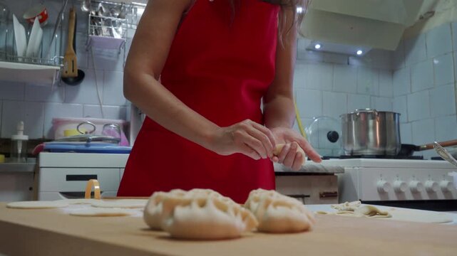 Close-up shows home cook shaping dumplings by hand on wooden board in warm domestic kitchen, sealing pleats beside simmering pot, with cozy indoor light and simple meal preparation mood
