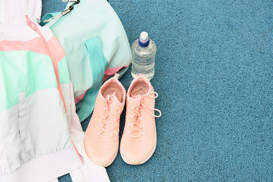 Pink athletic shoes, gym bag, and water bottle on a blue sports court, fitness and healthy lifestyle