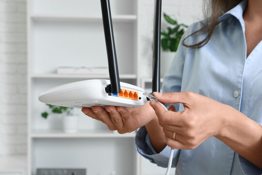 Woman connecting an ethernet cable to a white wireless router for internet access and network setup