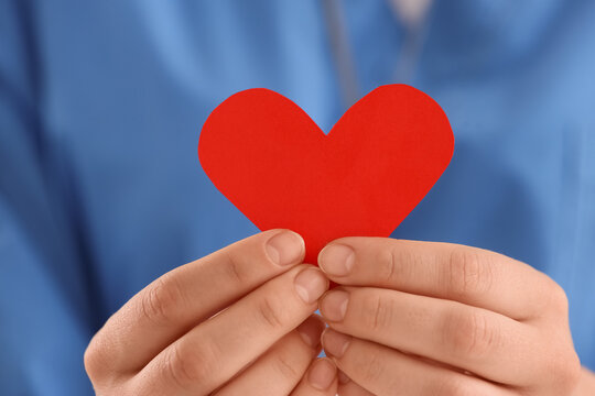 Hands holding a red paper heart, healthcare and medical support concept, charity and donation, blue background