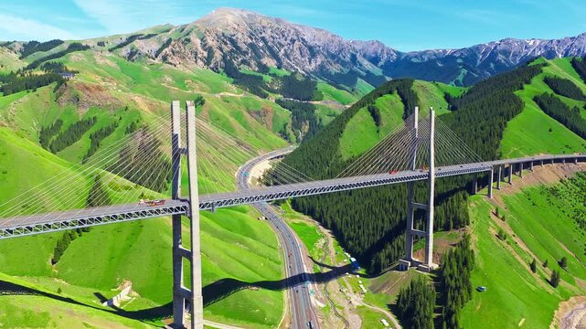 Aerial view of Guozigou Bridge spanning across lush green mountains in Xinjiang, China.