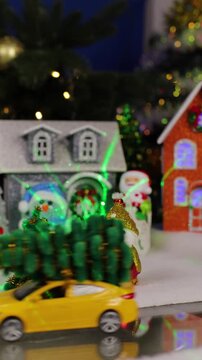 A yellow car pulls up to a large Christmas town with Christmas trees and snowmen near colorful houses