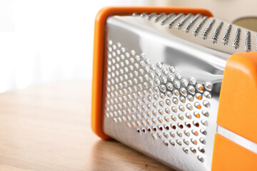 Stainless steel box grater with orange handle on a wooden table, kitchen utensil for food preparation, this kitchen utensil is essential for food preparation © Pixel-Shot