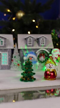 A yellow car with a Christmas tree on the roof drives up to a large Christmas town with Christmas trees and snowmen near colorful houses.