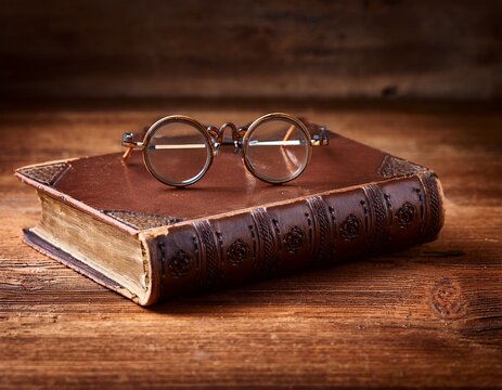 antique leather bound book and vintage glasses on wooden desk