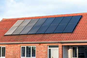 Fototapeta premium Solar panels on red tiled roof of brick house under blue sky