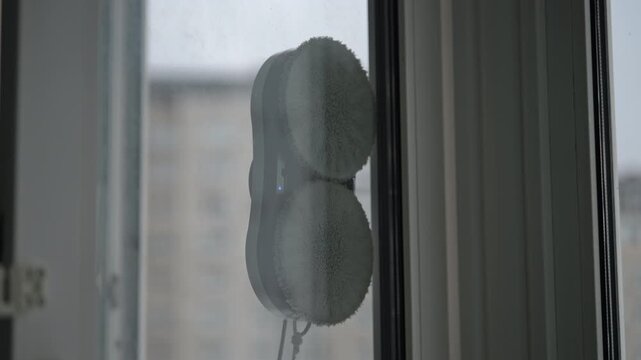 Close-up of smart home device with rotating microfiber pads washing dirty window. Automatic robot helper for cleaning glass surfaces. Concept of modern technology simplifying housekeeping tasks.