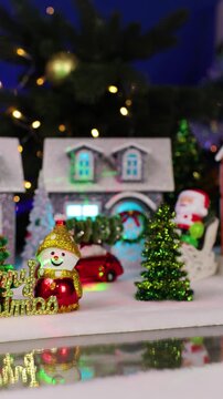 In the foreground of a large Christmas town are two snowmen with letters