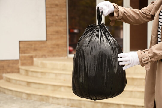 Young woman with garbage bag near building on street, closeup
